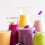 6 healthy breakfast smoothies of different colors in different sized glass jars
