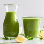 green smoothie in jug and jar with lemon and cilantro around