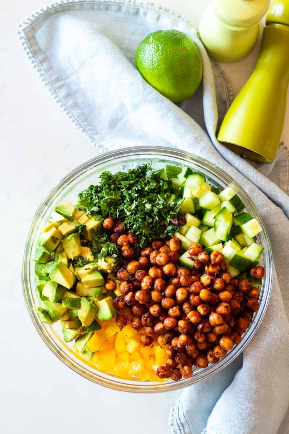 Cucumber Avocado Salad with crispy spicy chickpeas in a glass bowl next to a pale blue napkin