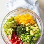 Cucumber Tomato Avocado Salad ingredients in a large glass bowl and balsamic vinaigrette in a separate glass jar