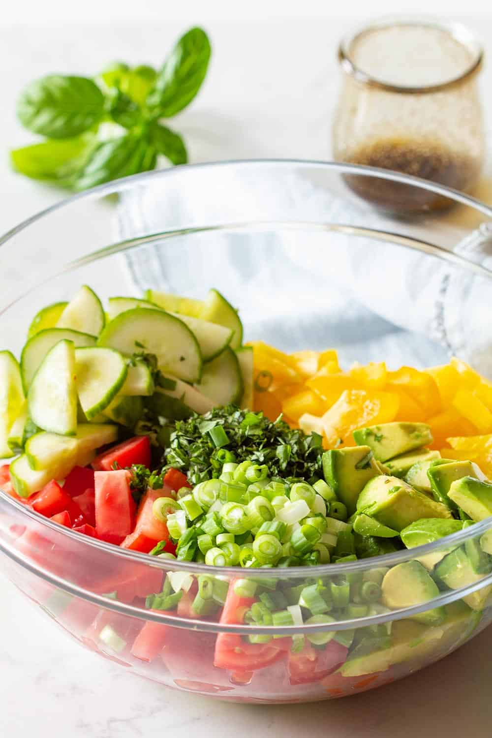 Cucumber Tomato Avocado Salad Recipe in a glass bowl and balsamic vinaigrette in a separate glass jar