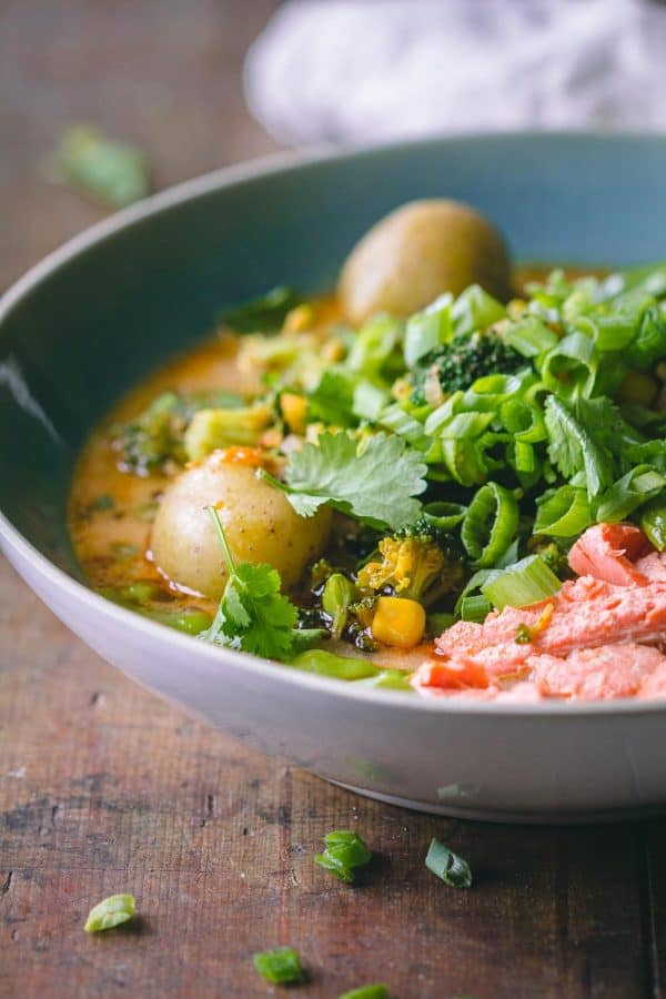 Thai Curry Soup in a blue bowl showing shredded salmon, potatoes, broccoli, and snow peas in broth