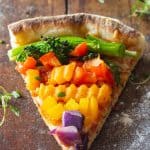 A piece of authentic Italian veggie pizza with veggies of the colors of the rainbow.