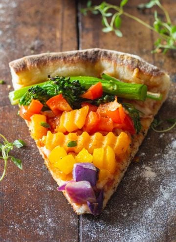 A piece of authentic Italian veggie pizza with veggies of the colors of the rainbow.