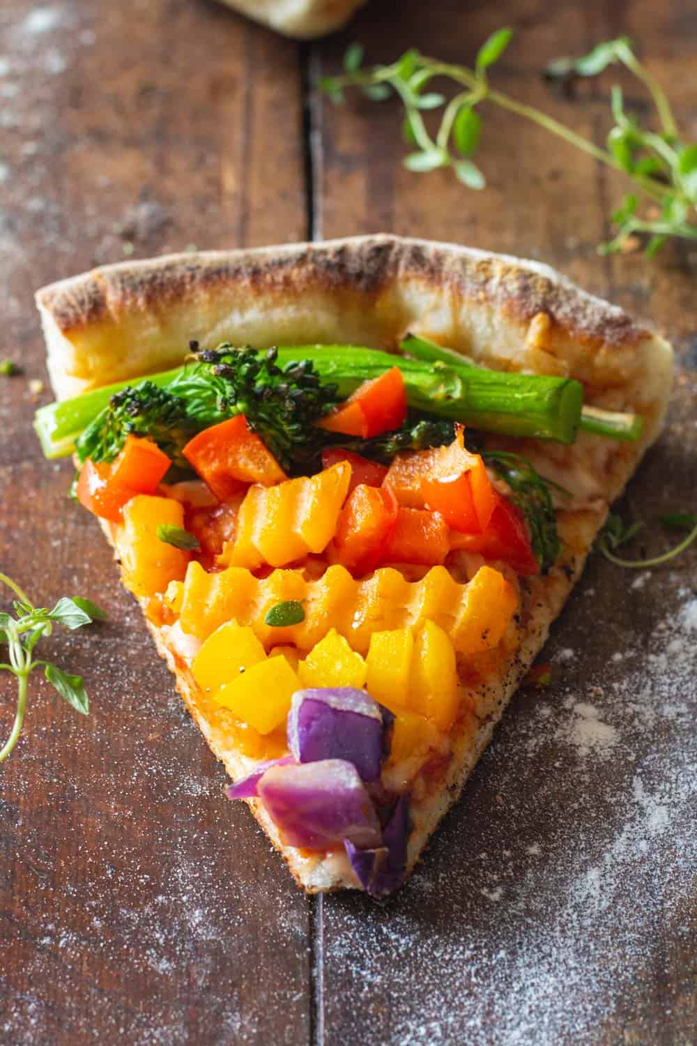 A piece of authentic Italian veggie pizza with veggies of the colors of the rainbow.