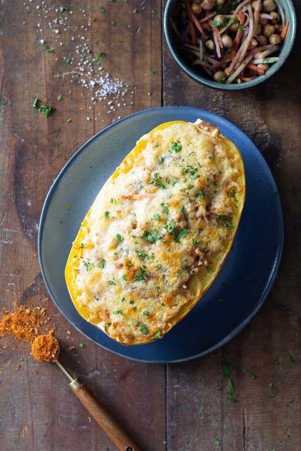 Half stuffed spaghetti squash with melted cheese on top on a blue plate