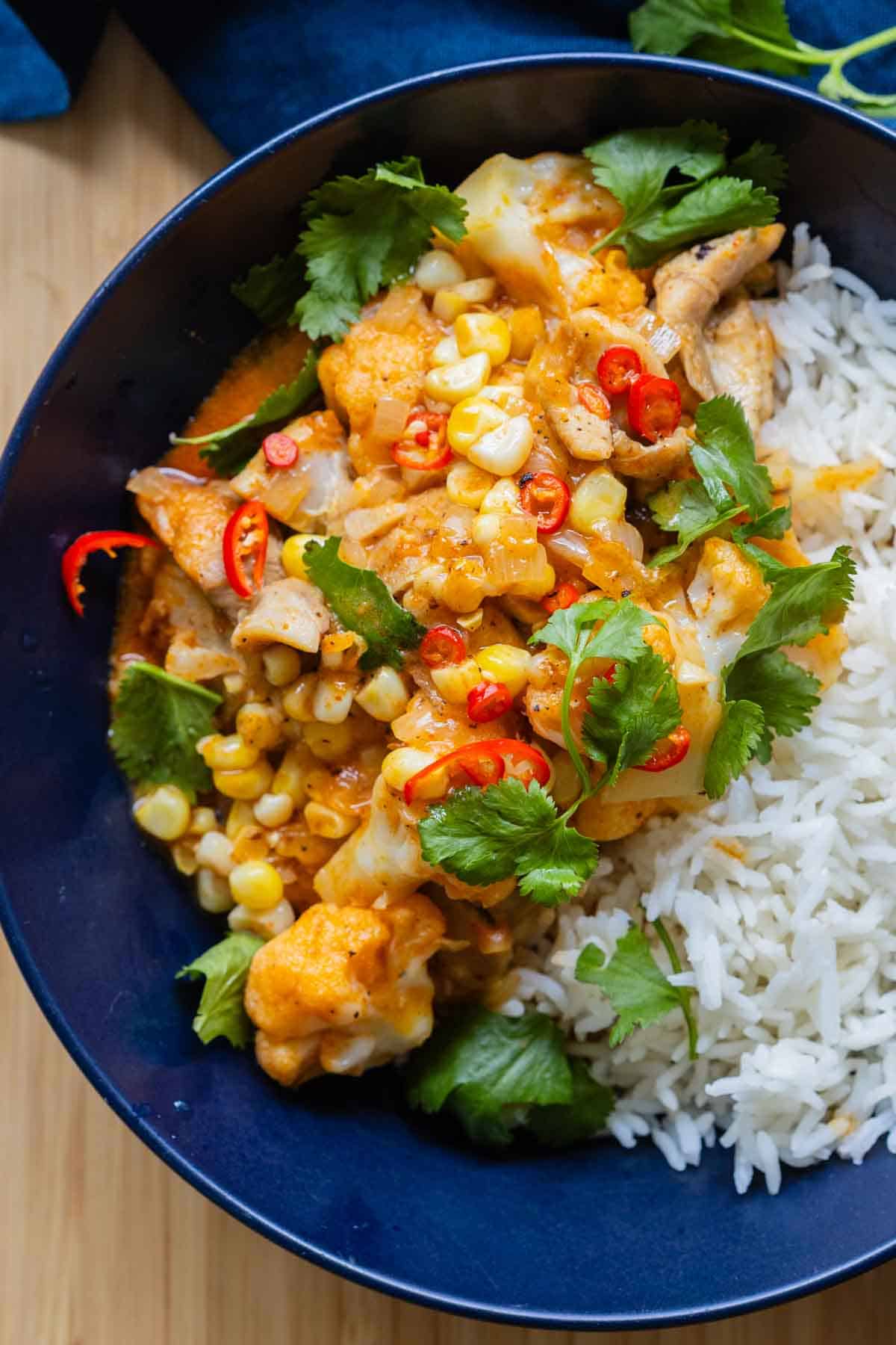 Thai Chicken Cauliflower Curry next to white rice in a blue serving bowl.