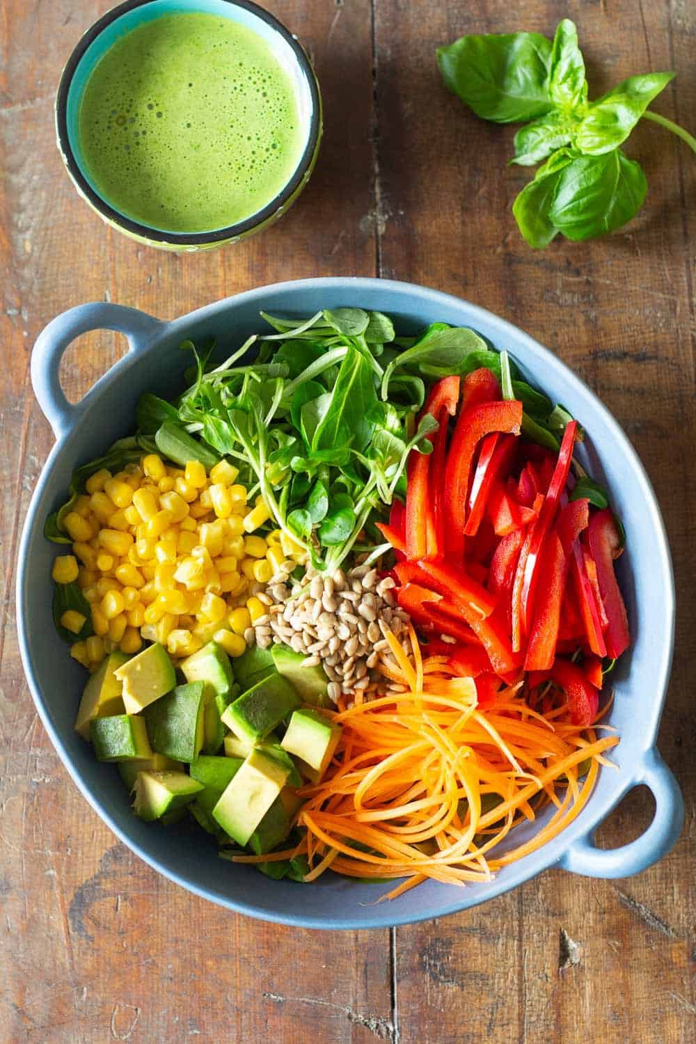 Ingredients for healthy summer salad with fresh vegetables in a light blue salad bowl, and a cup of orange basil vinaigrette.