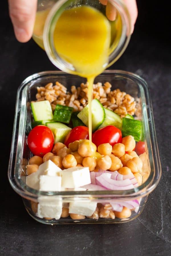 Pouring lemon tahini dressing over vegetarian meal prep bowl