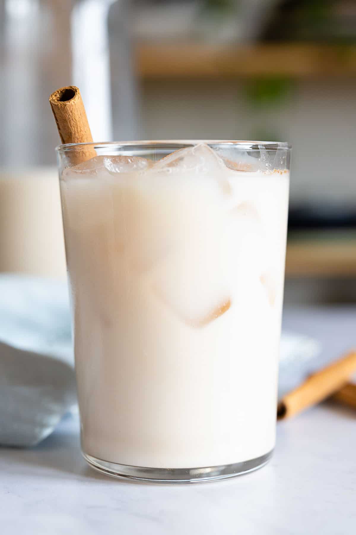 Agua de Horchata in a glass with ice and cinnamon stick sticking out.