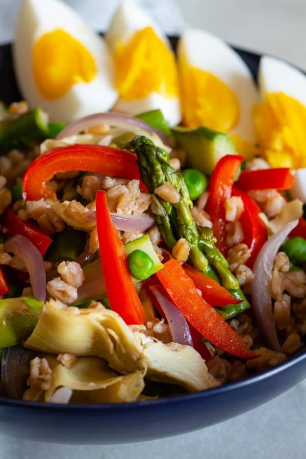 healthy spring salad with spring vegetables, hard boiled egg wedges, and farro