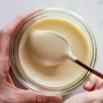 jar with homemade mayonnaise and hands holding it with spoon in mayonnaise