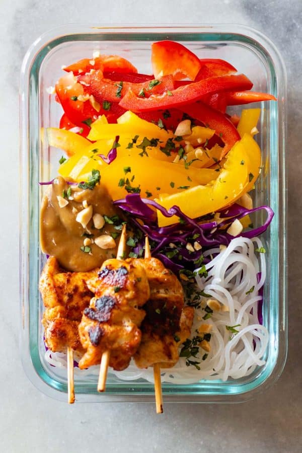 Chicken Satay on wooden skewers with raw vegetables served on rice noodles with peanut sauce