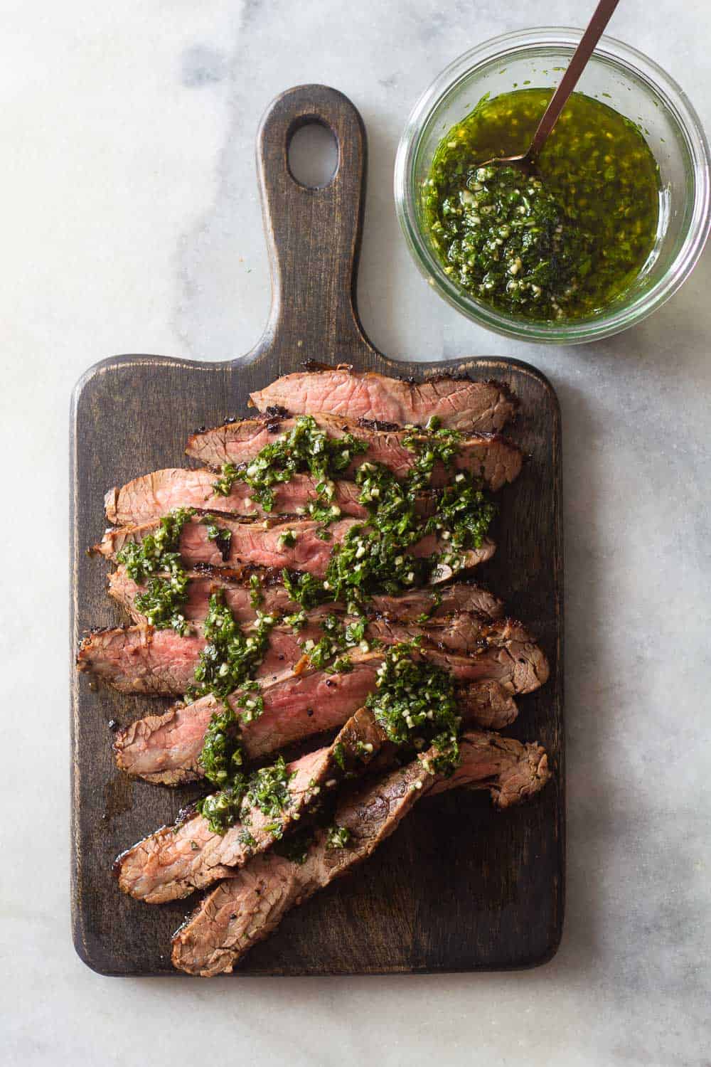 Flank Steak on a cutting board and Chimichurri in a jar