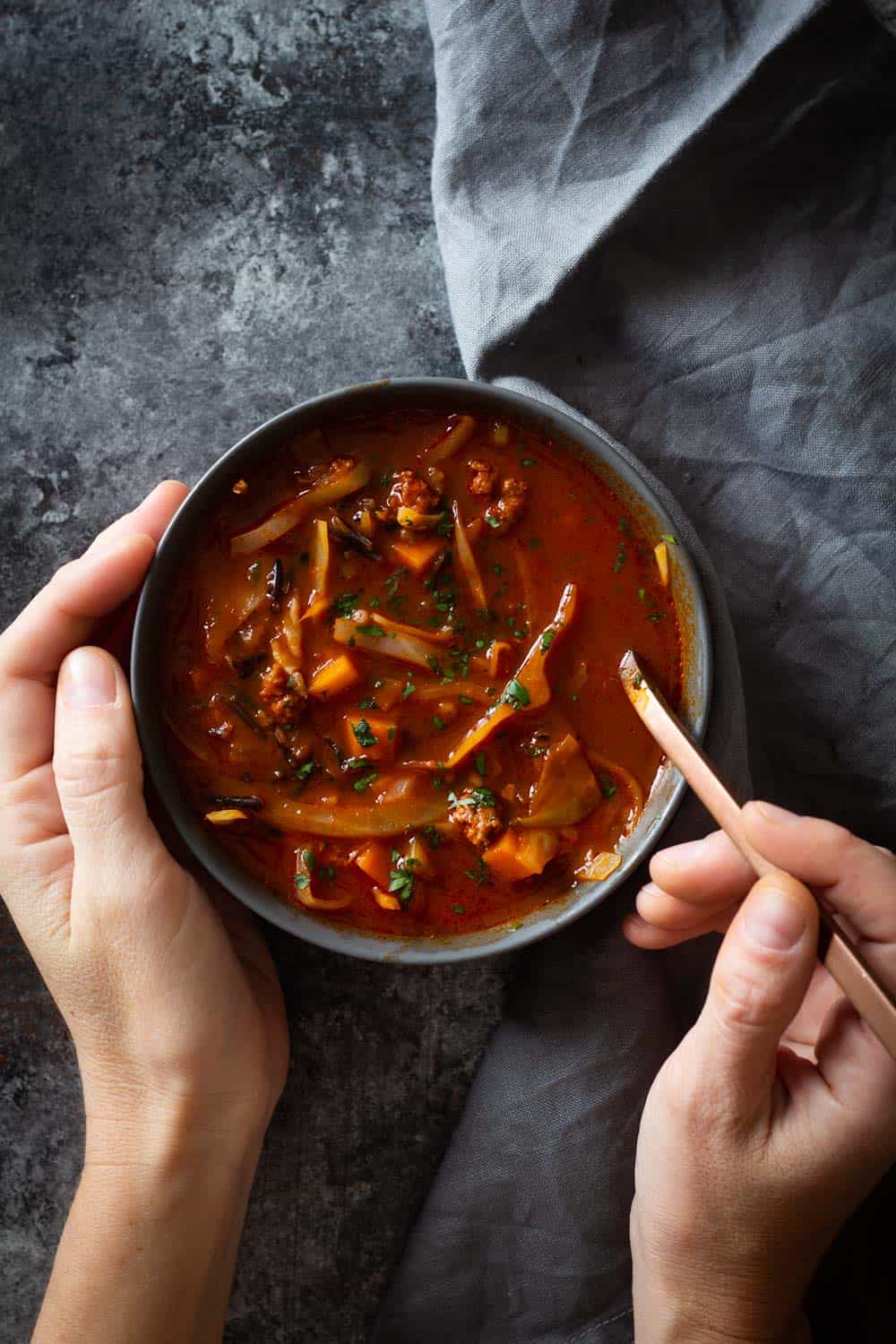 Cabbage Roll Soup in a bowl with hands holding bowl and spoon