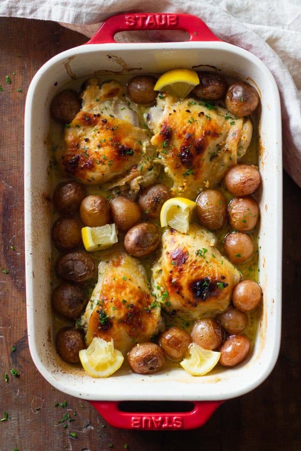 Lemon Garlic Chicken in Baking Dish with baby potatoes and lemon wedges