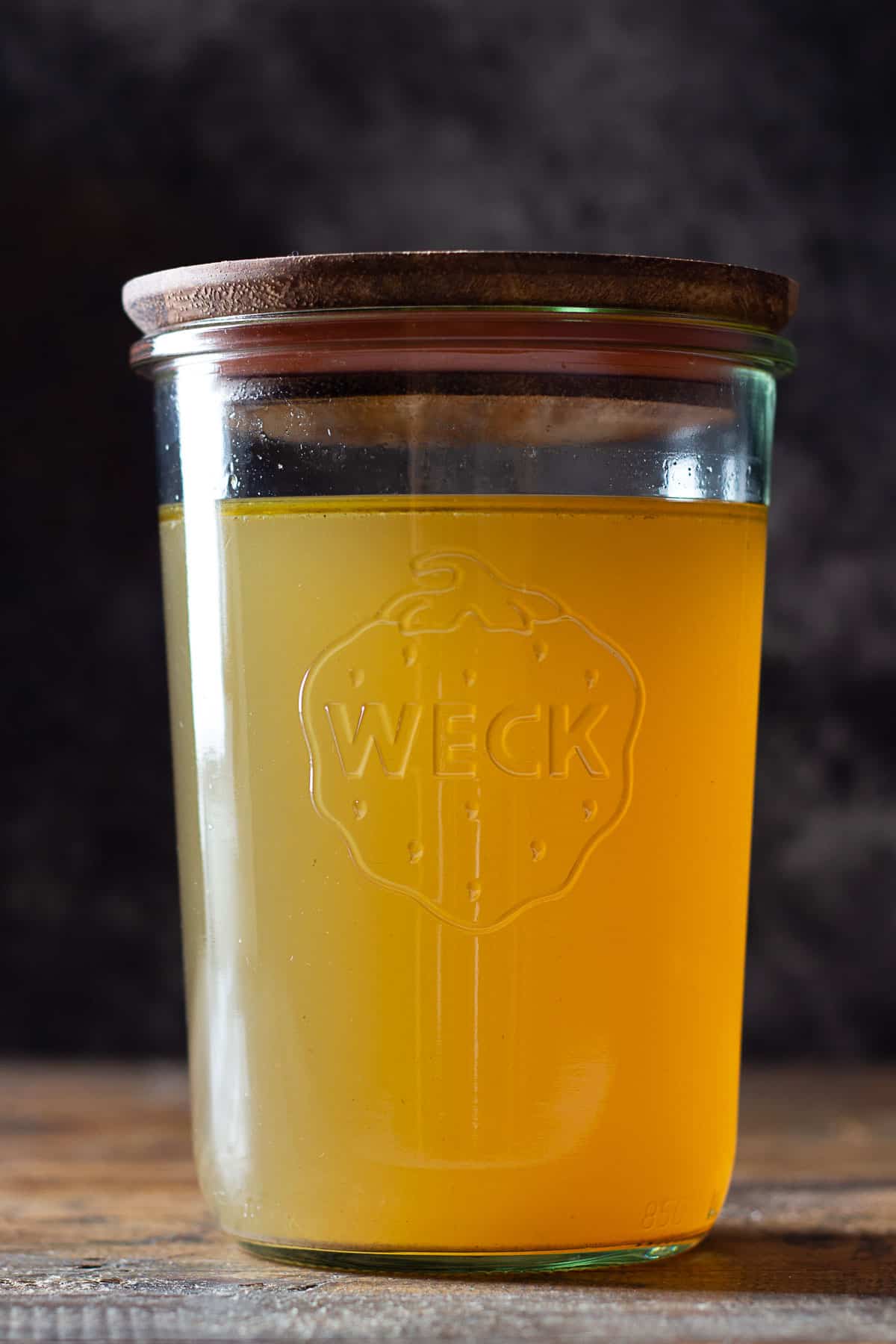 Golden chicken bone broth in a glass jar with wooden lid on top