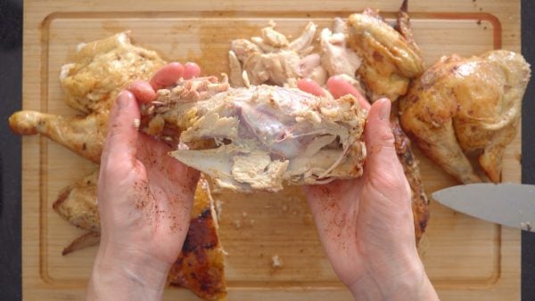 Chicken carcass held in hands over a wooden board