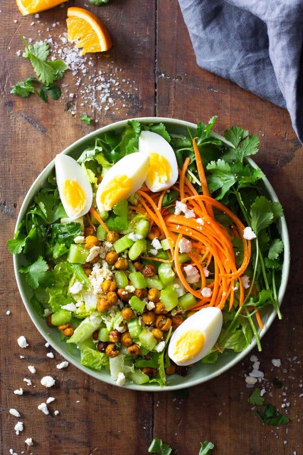 green salad topped with carrots, chickpeas, feta, and cut-up hard boiled egg in a bowl