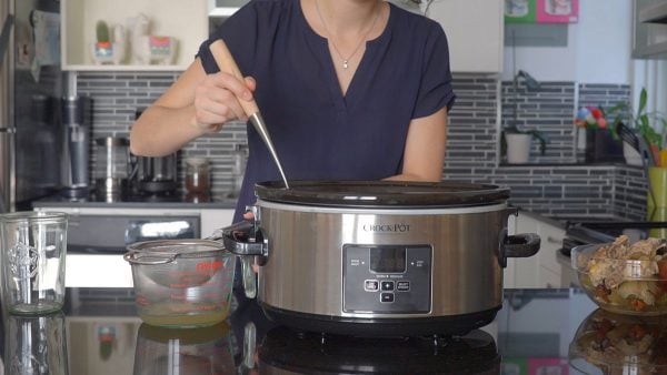 Person holding ladle inside slow cooker bowl with sieve next to slow cooker