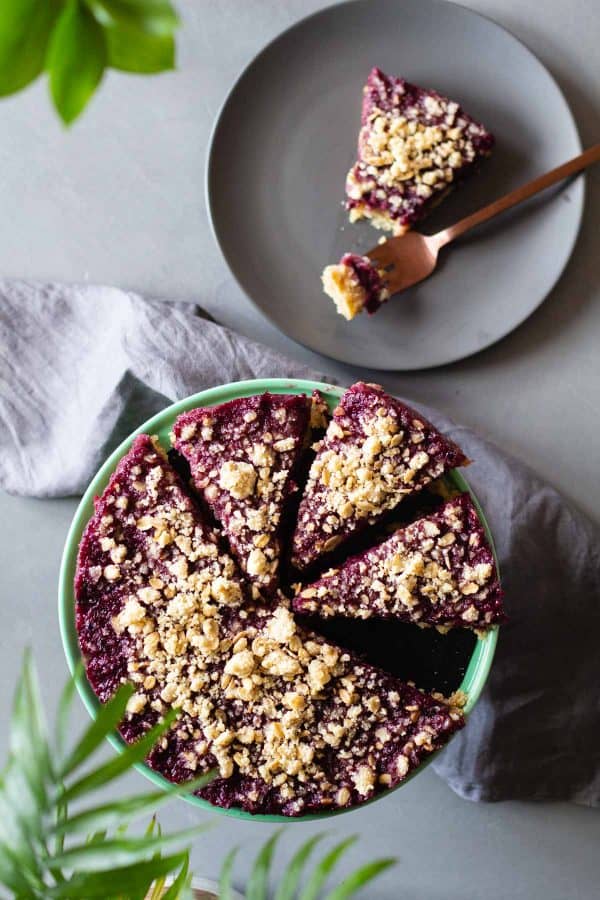 Blackberry Pie on a green cake stand and plate with 1 piece of pie and a fork