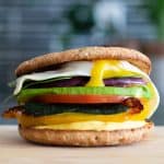 multi-layered sandwich with different colored vegetables and a fried egg on top on a cutting board