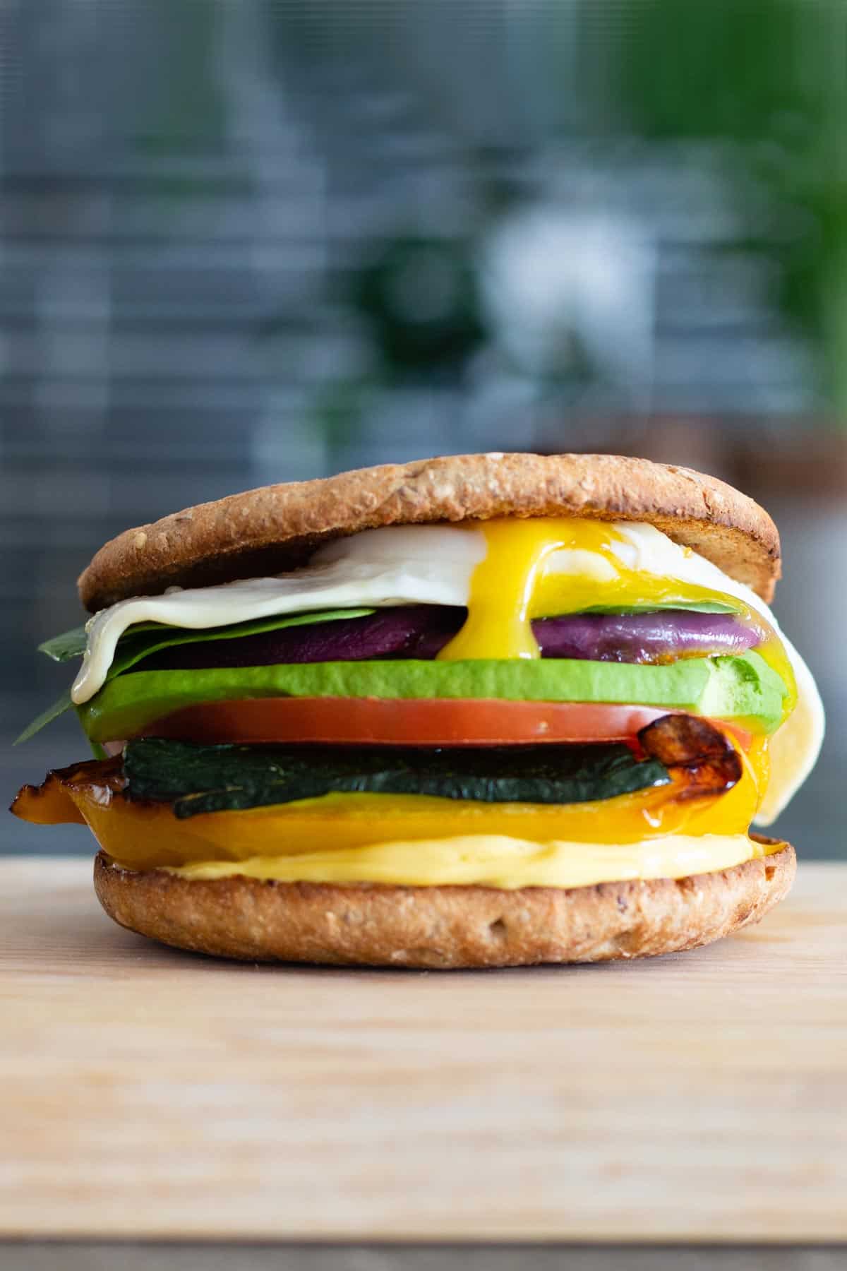 multi-layered sandwich with different colored vegetables and a fried egg on top on a cutting board