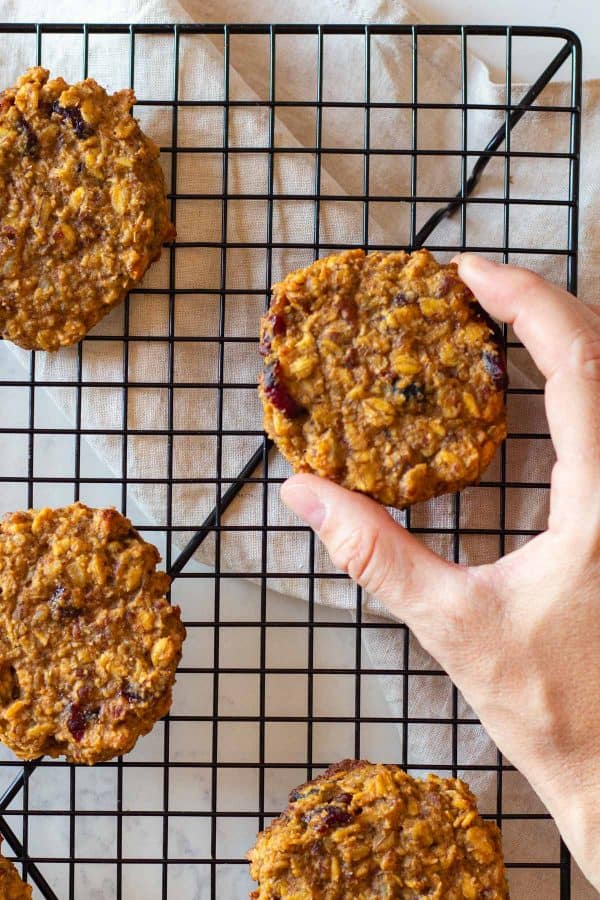 Hand grabbing an oatmeal cookie from a cooling rack.