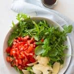 arugula, diced tomato, and shaved parmesan in a white salad bowl