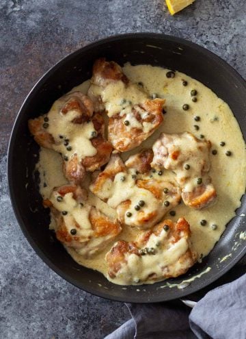 Chicken Thighs in a pan with creamy sauce and green pepper corns on top.