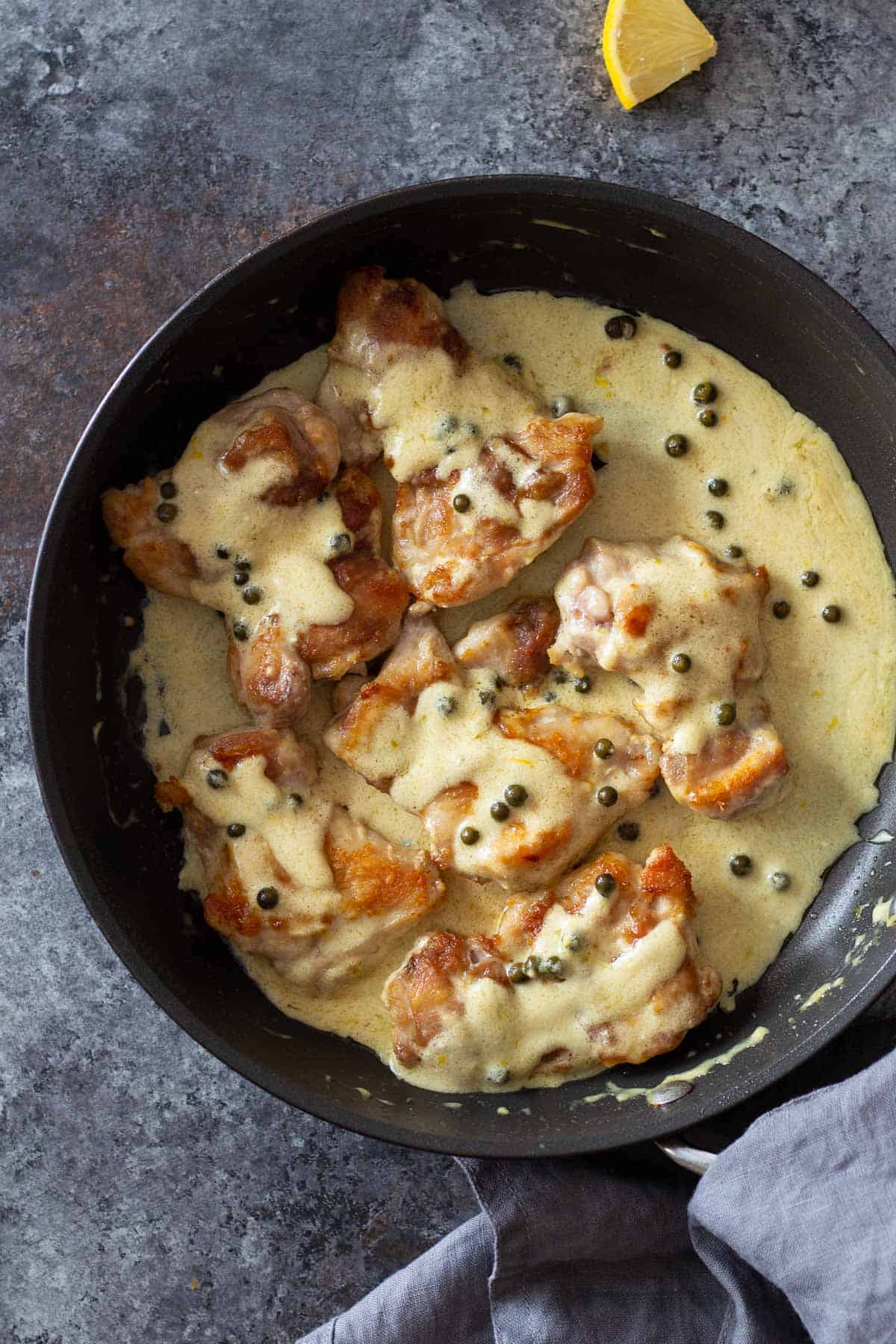 Chicken Thighs in a pan with creamy sauce and green pepper corns on top.