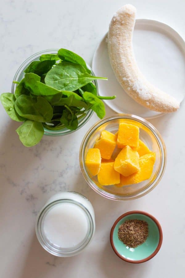 frozen banana, spinach, mango chunks, coconut milk, ground flaxseeds on a kitchen counter