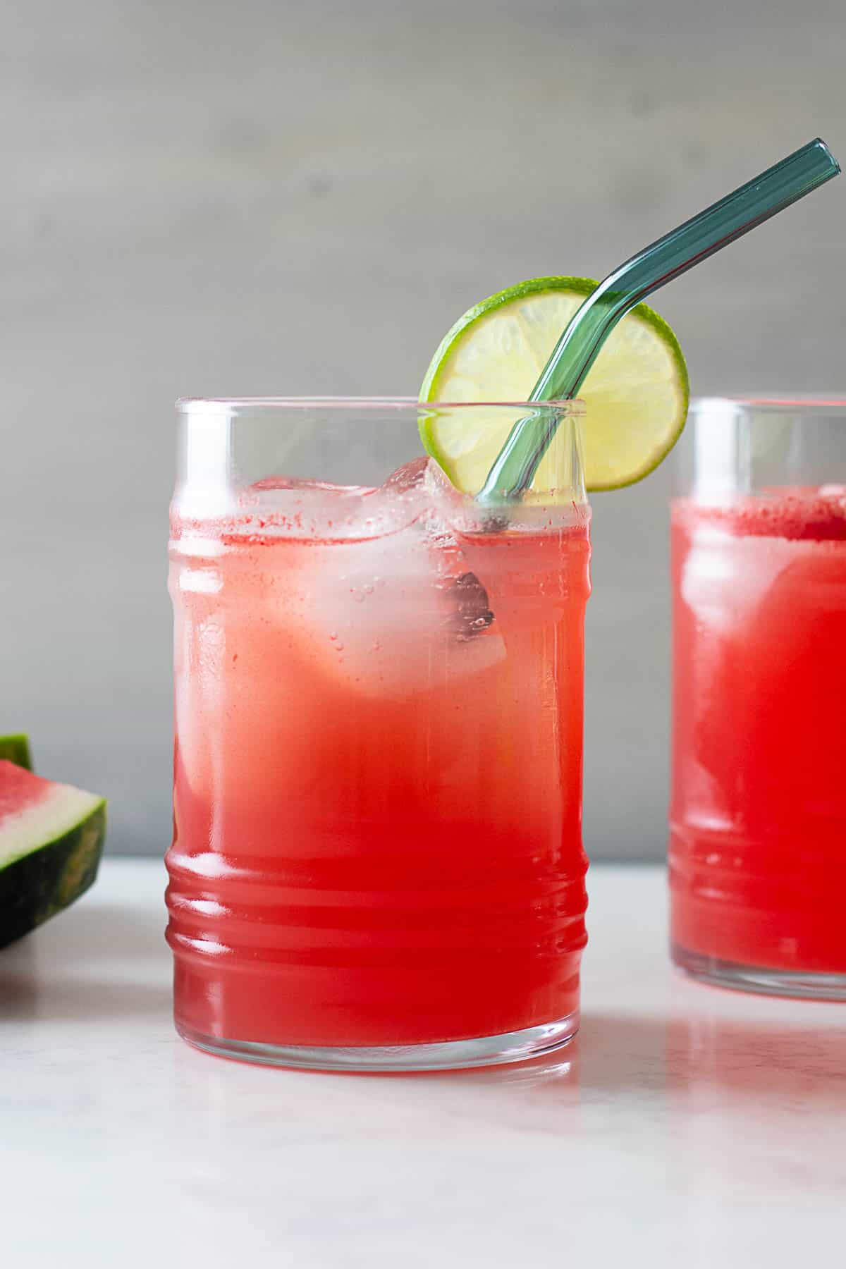 watermelon agua fresca in a glass with lime slice at edge and blue glass straw