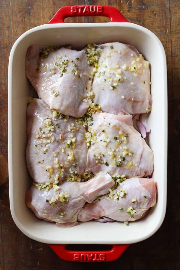 Raw chicken thighs and drumsticks with garlic rosemary lemon sauce on top in an ovenproof dish.