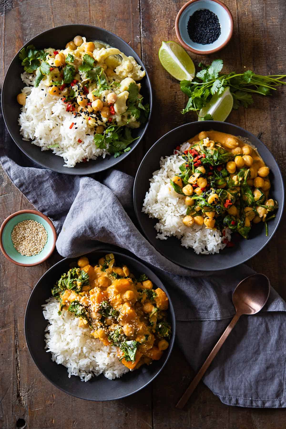 Three bowls with white rice and different kinds of coconut chickpea curry.