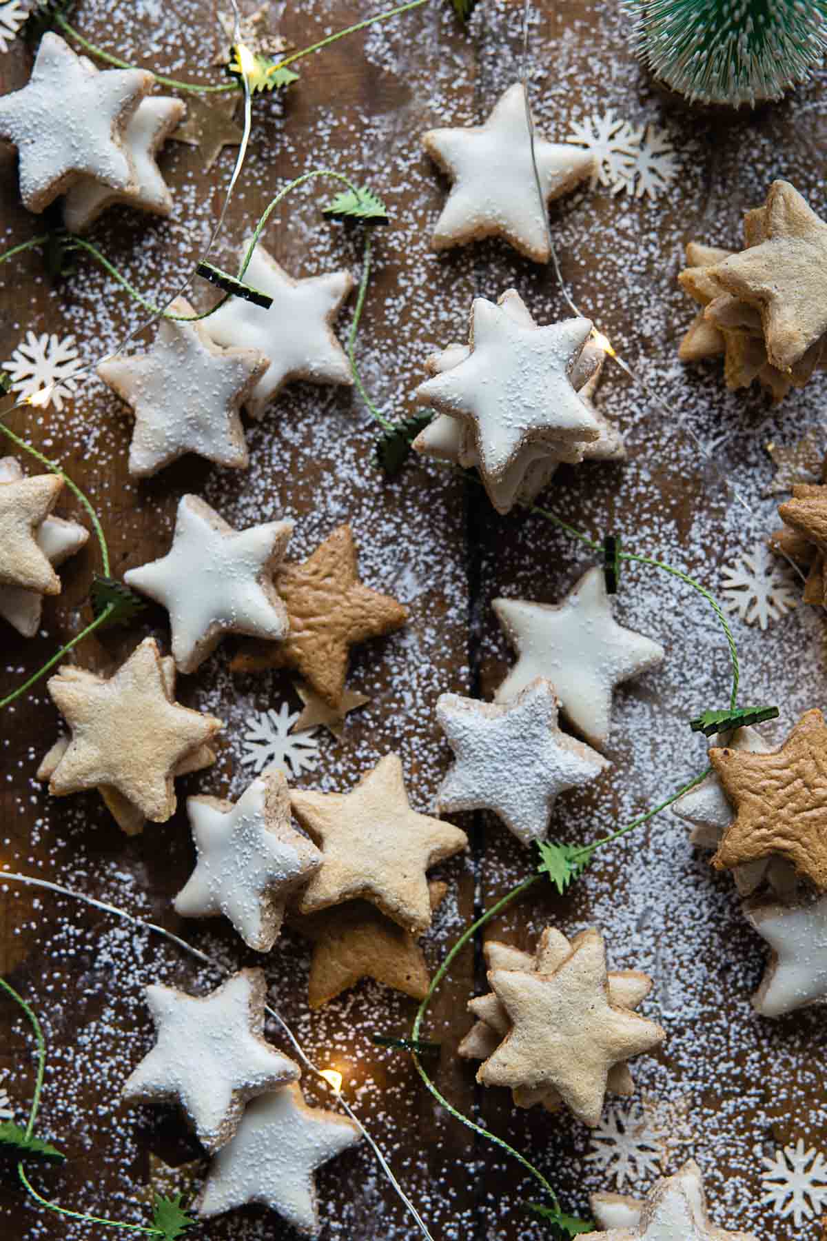 A lot of Zimtsterne, regular, paleo, and vegan, laying on a wooden table dusted with powdered sugar.