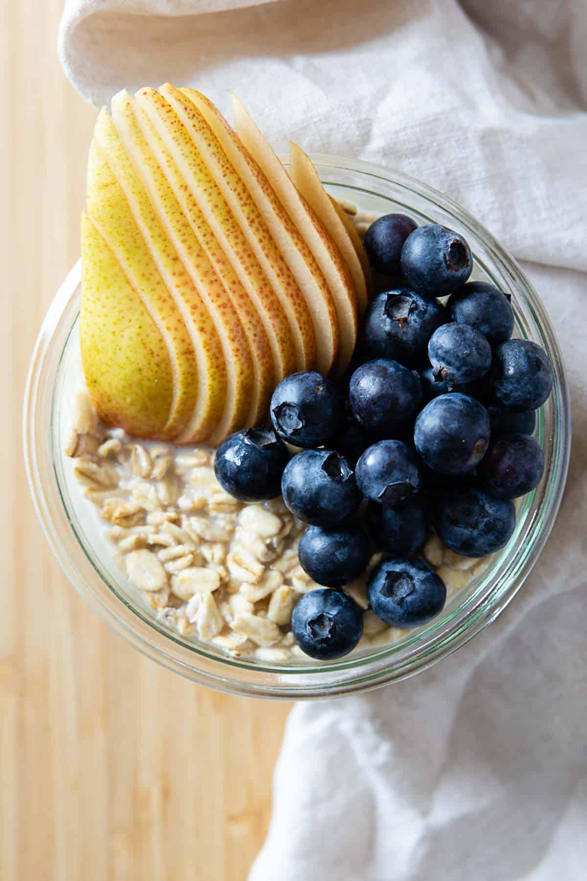 Overnight oats in a glass jar topped with sliced pear and blueberries.