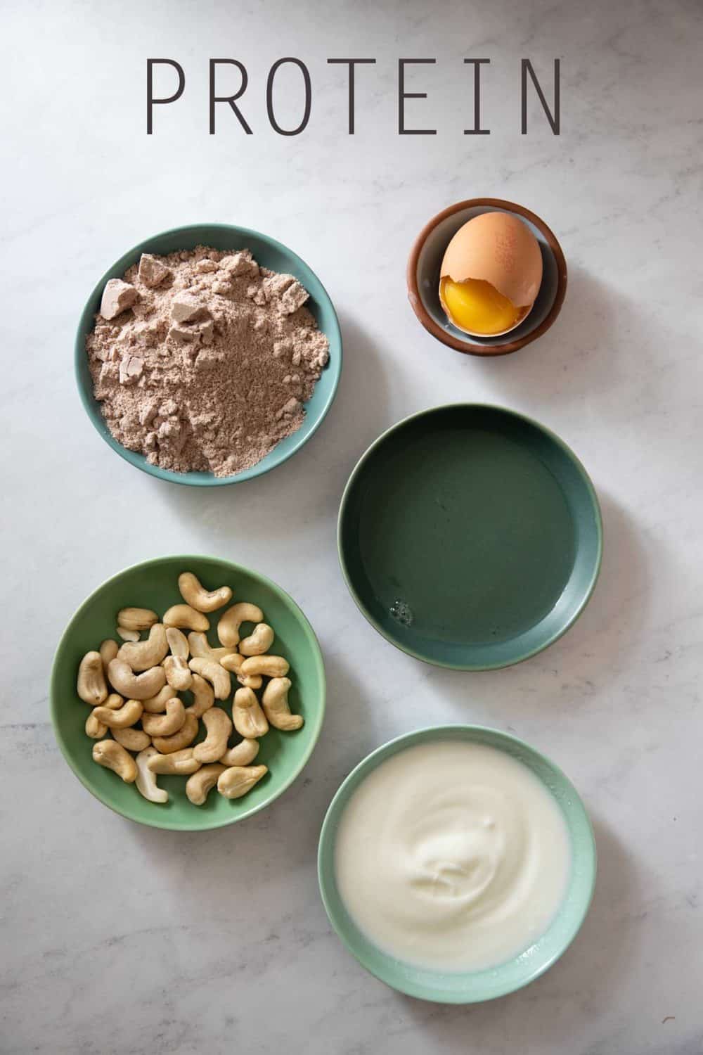 Yogurt, cashews, protein powder, egg white, egg shell with egg yolk in 5 little bowls.