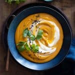 Red Lentil Sweet Potato Soup in blue bowl with swirl of sour cream.