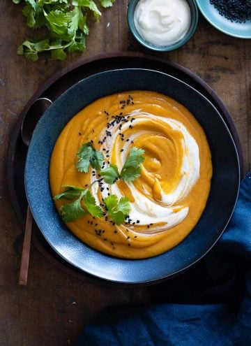 Red Lentil Sweet Potato Soup in blue bowl with swirl of sour cream.