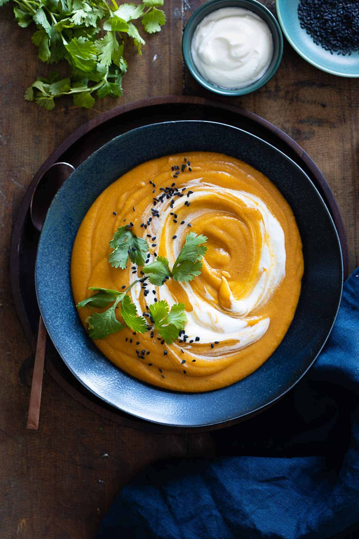 Red Lentil Sweet Potato Soup in blue bowl with swirl of sour cream.