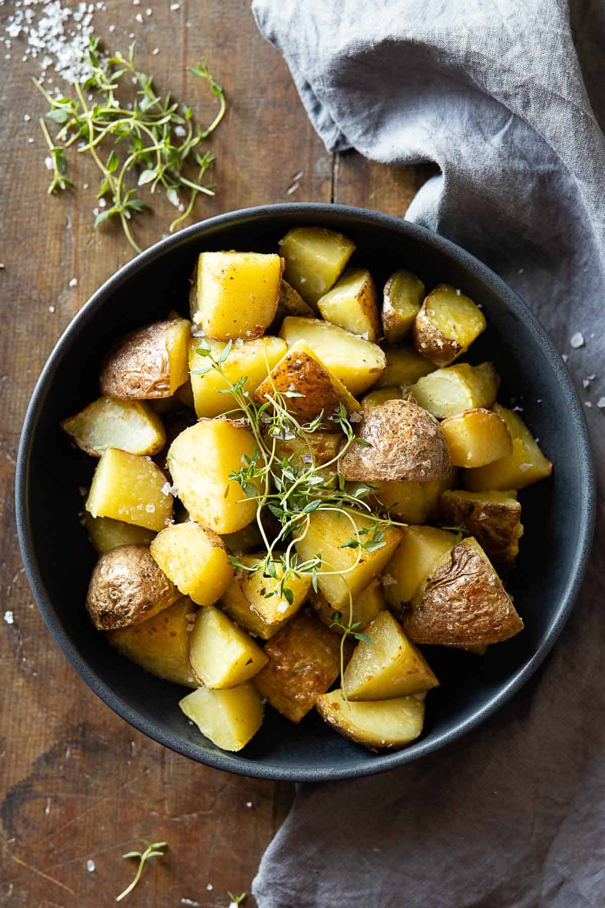 Cooked cut up red potatoes in a grey bowl garnished with fresh thyme.