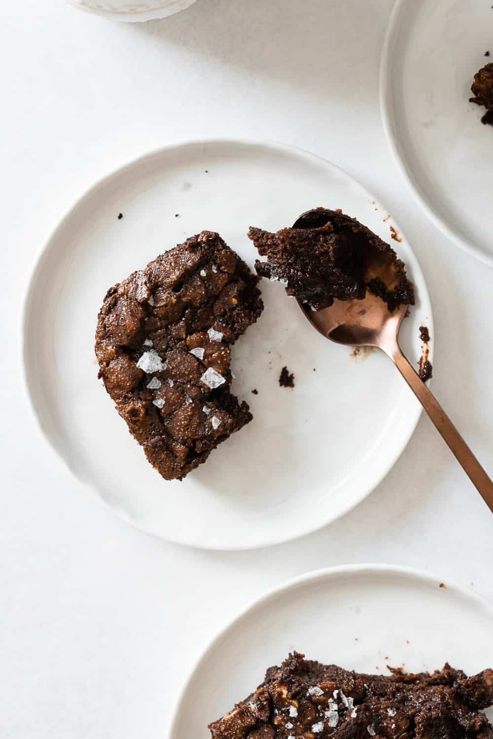 Piece of paleo brownie recipe on a plate with dirty spoon next to it.