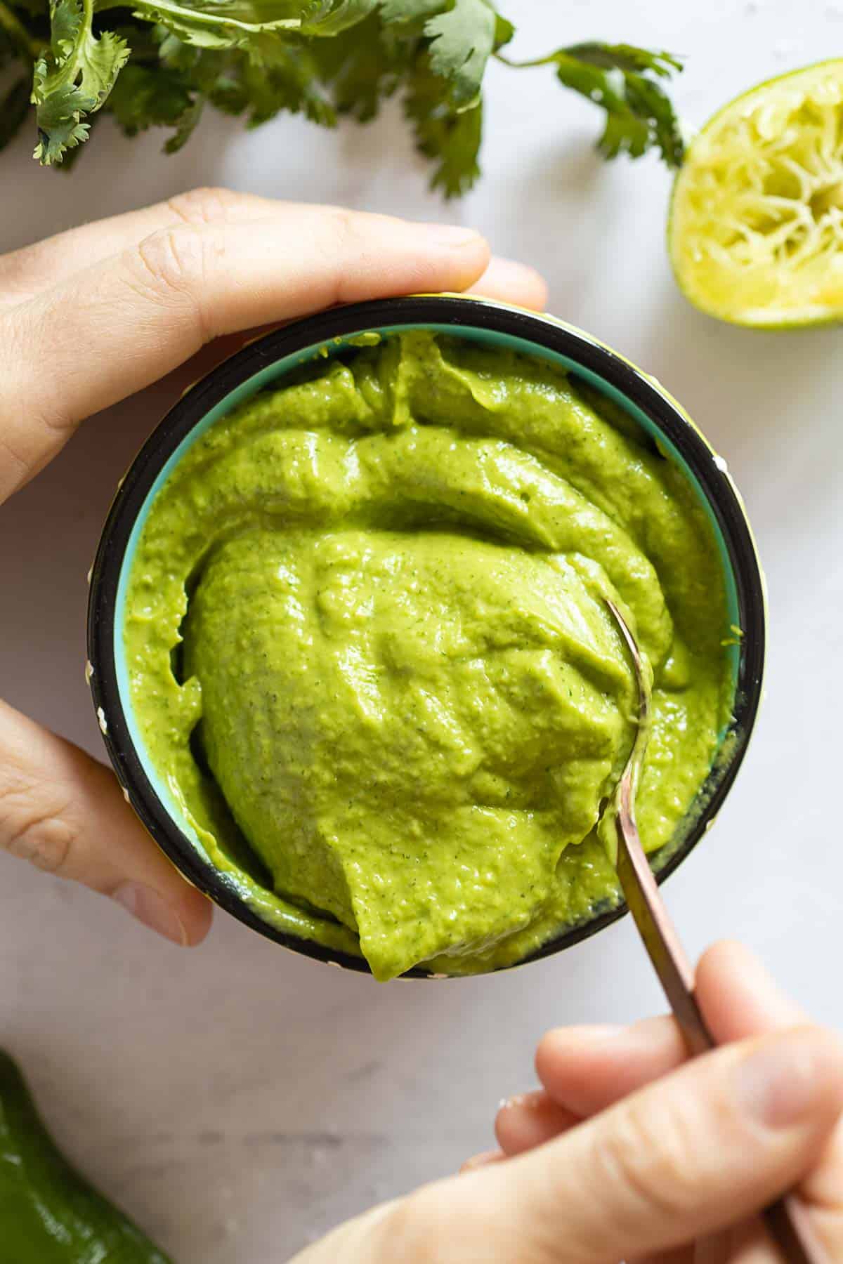 Avocado Dip in a bowl with a hand scooping out a spoon.