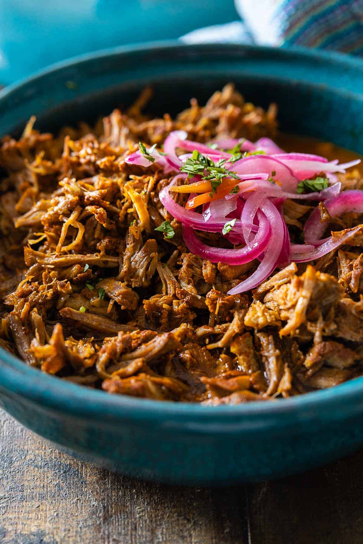 Closeup look of texture of Cochinita Pibil served in a blue bowl and topped with red onion.