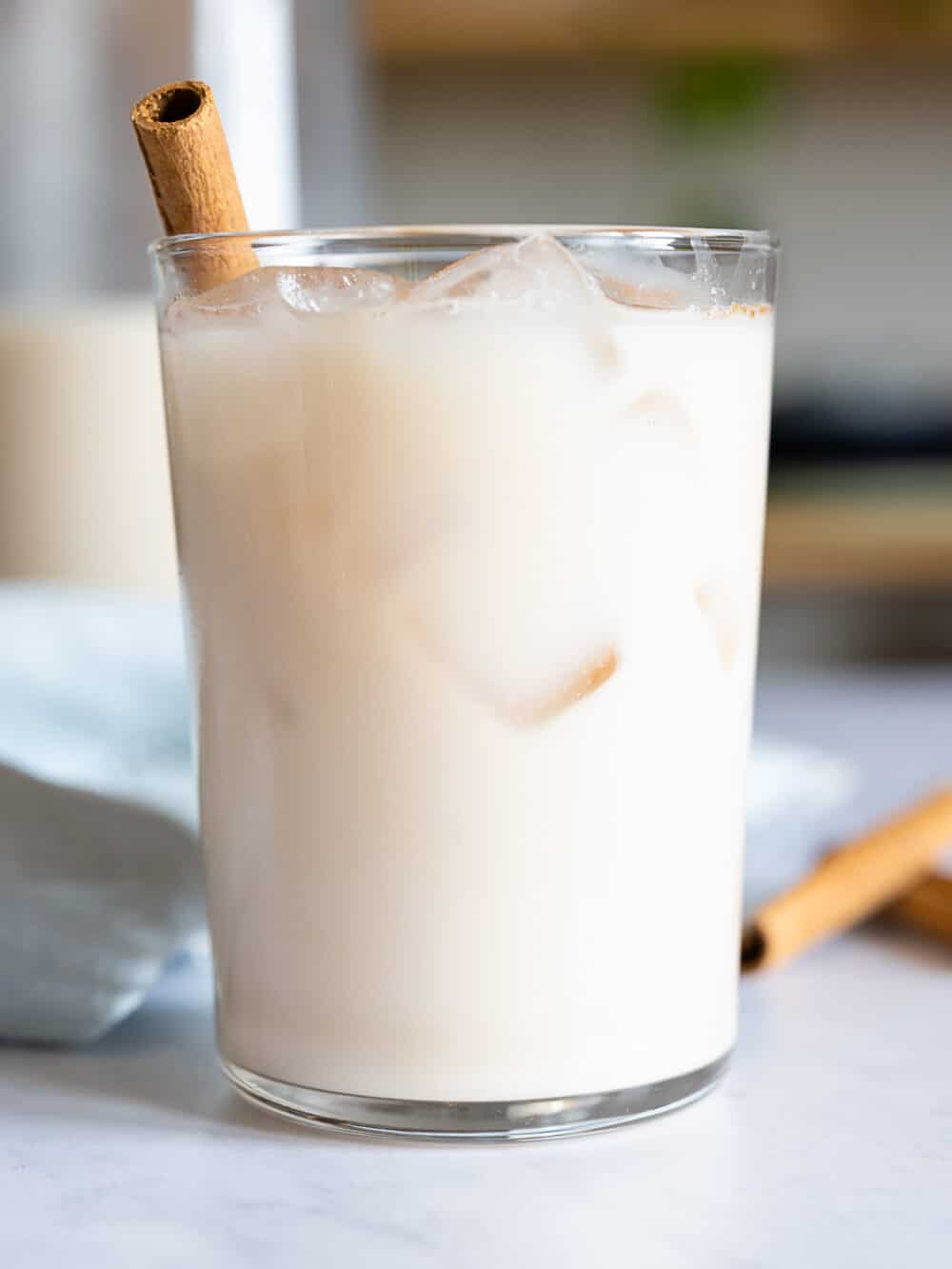 Agua de Horchata in a glass with ice cubes and cinnamon stick sticking out.