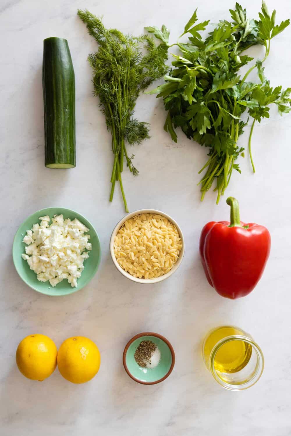 9 Ingredients for Orzo Salad laid out on a kitchen counter.