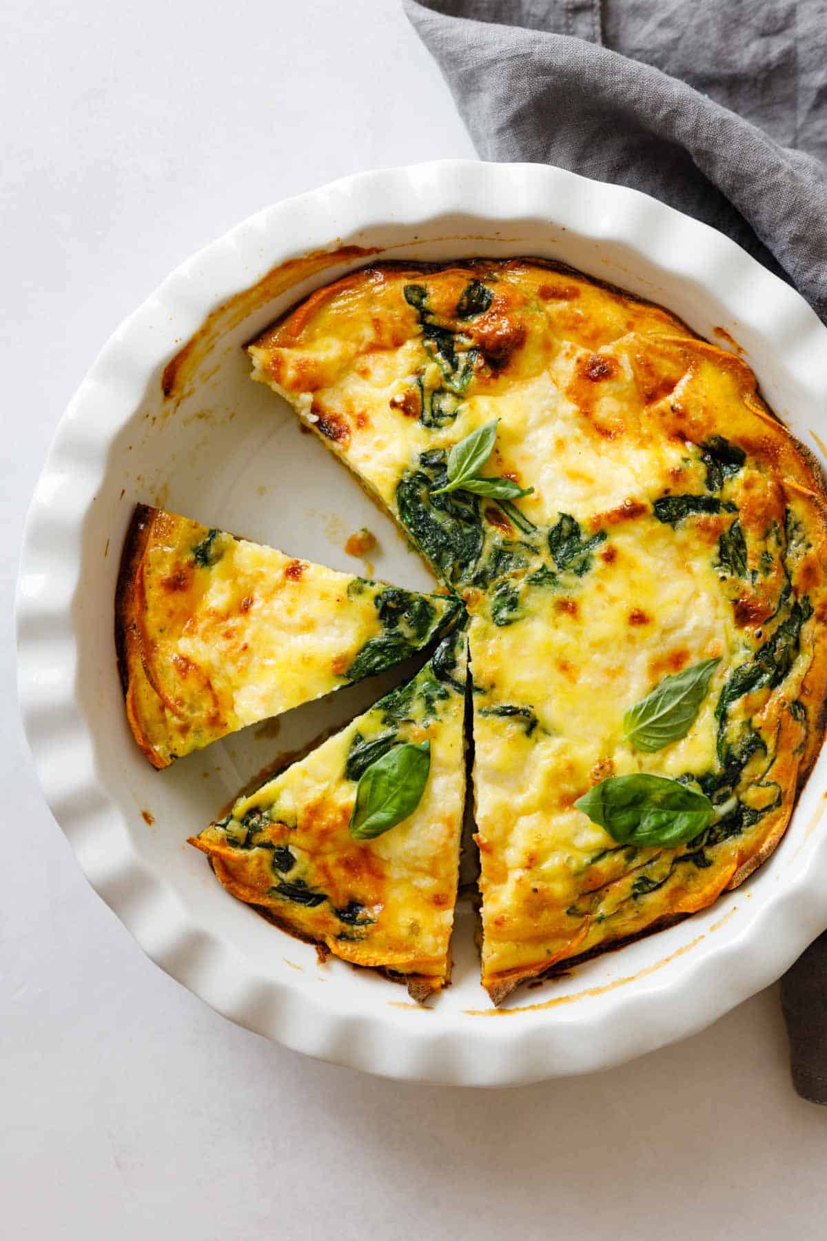 Crustless Spinach Quiche in a pie dish one piece missing two pieces cut out.