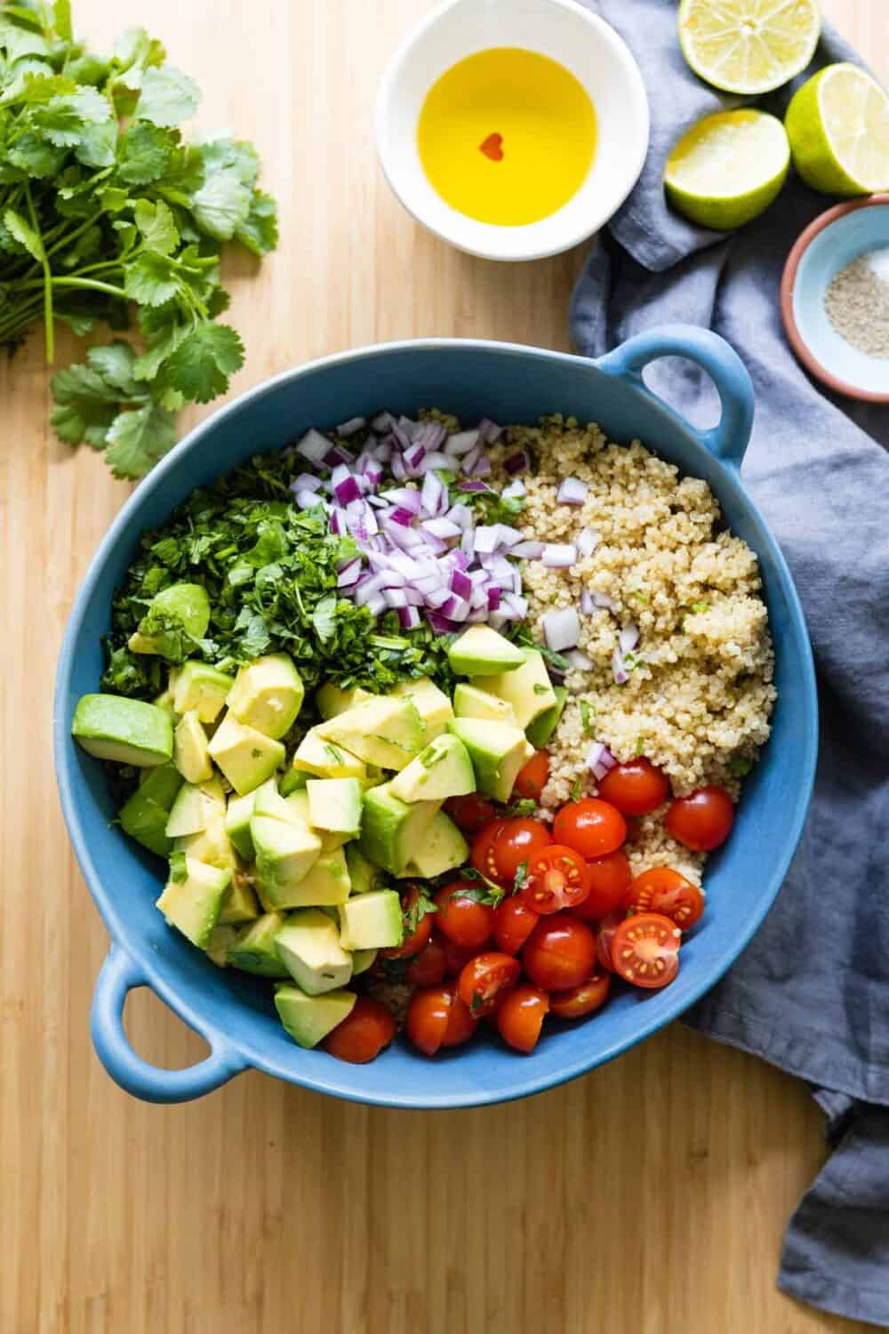 quinoa, avocado, cherry tomatoes, cilantro and red onion in a blue salad bowl.