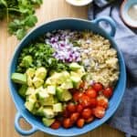 quinoa, avocado, cherry tomatoes, cilantro and red onion in a blue salad bowl.